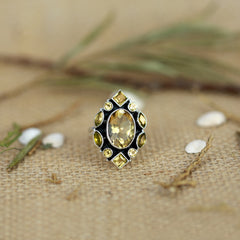 Ring with a yellow gemstone on a textured beige surface with greenery
