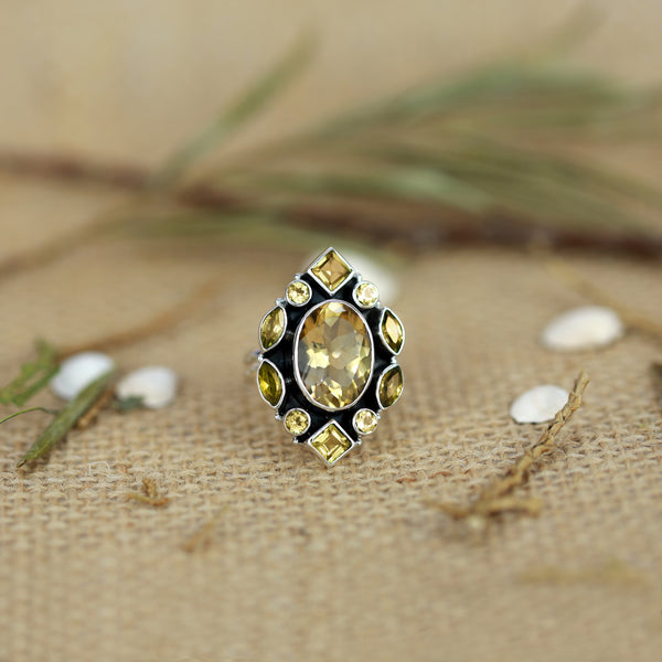 Ring with a yellow gemstone on a textured beige surface with greenery